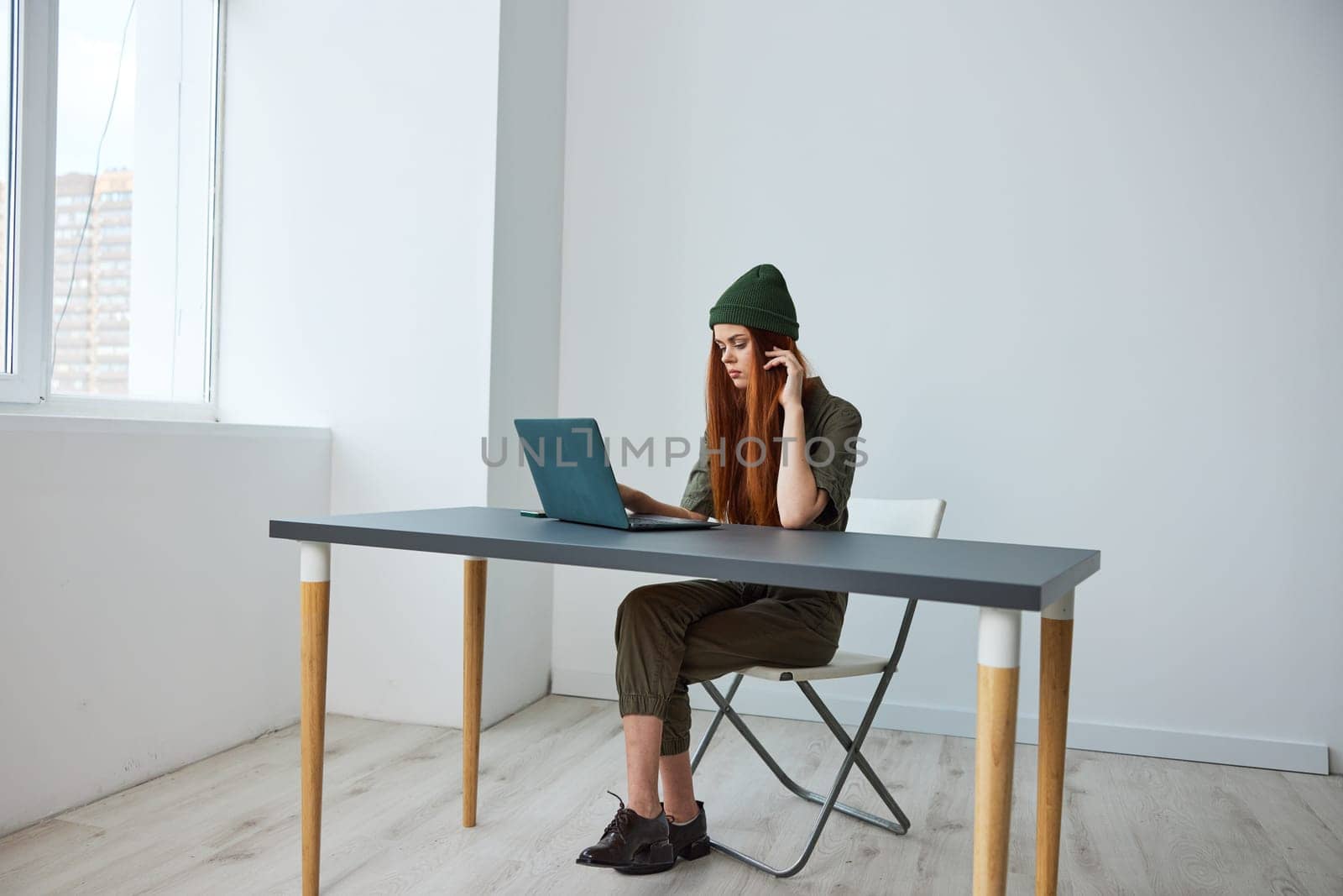 woman working in the office sitting at a table with a laptop in a hat. High quality photo