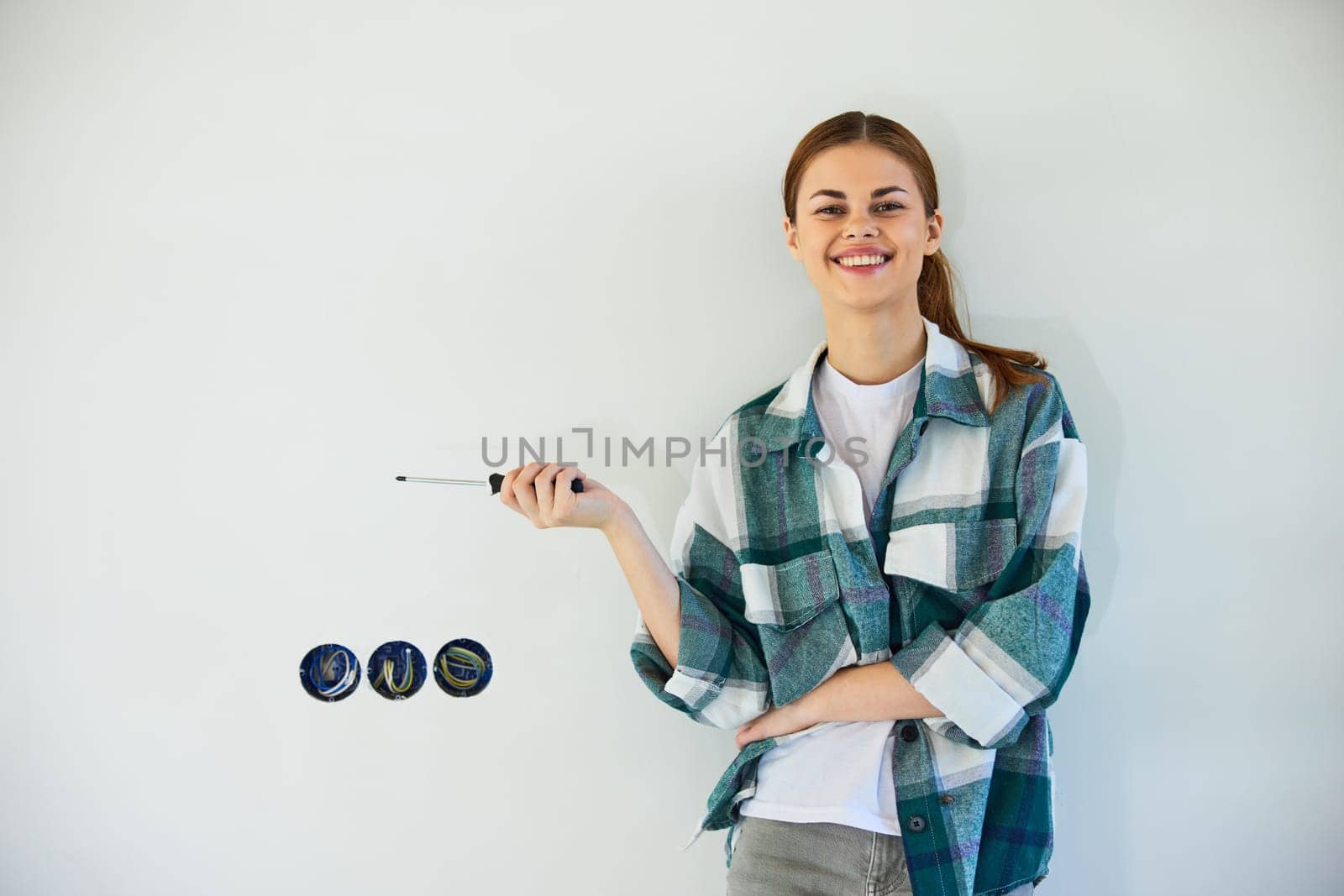 happy, smiling woman stands with a screwdriver and fixes sockets on a light wall. High quality photo