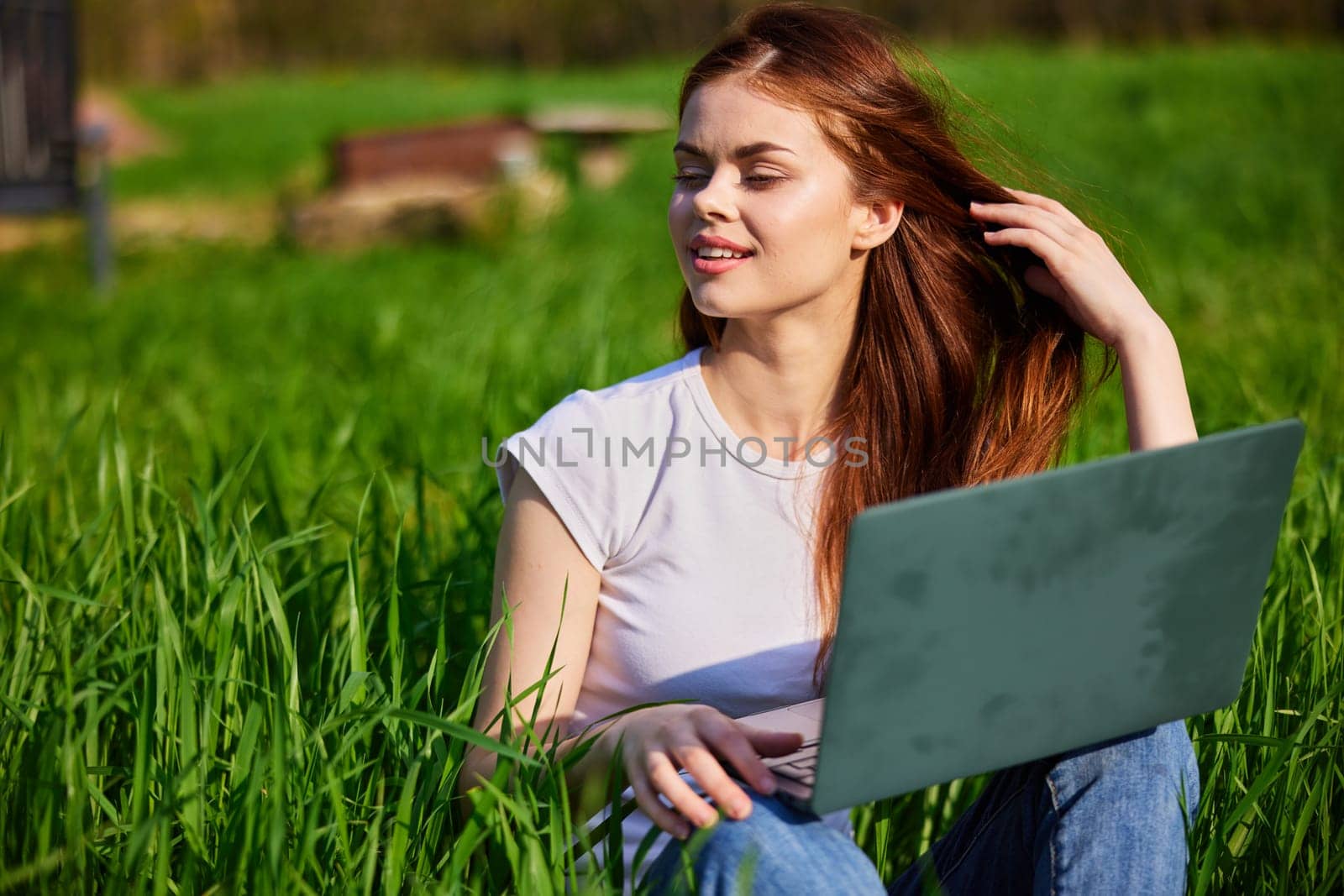 portrait of a woman sitting at a laptop in a field with a laptop in her hands by Vichizh