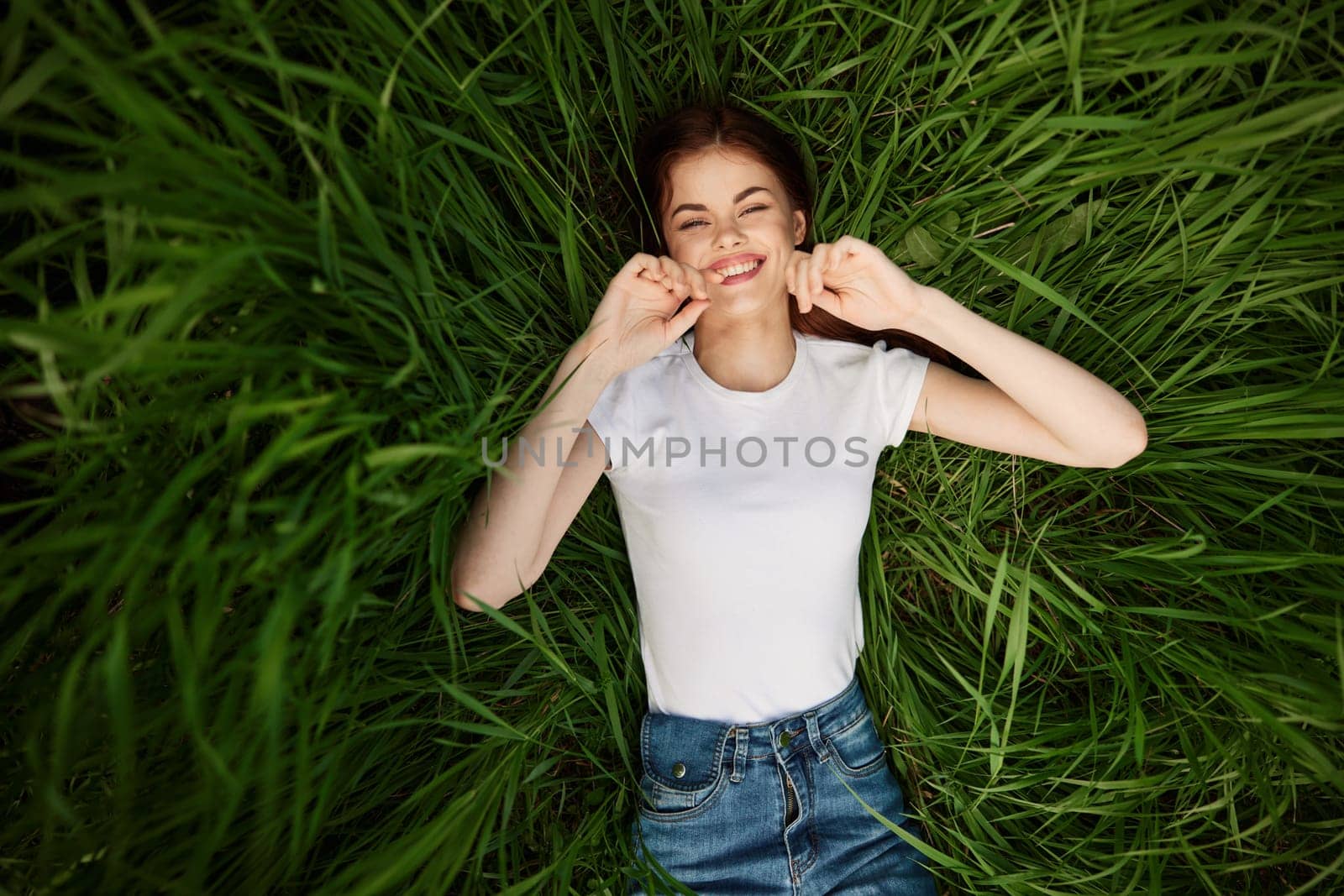 a woman with even, white teeth laughs in the green grass. High quality photo