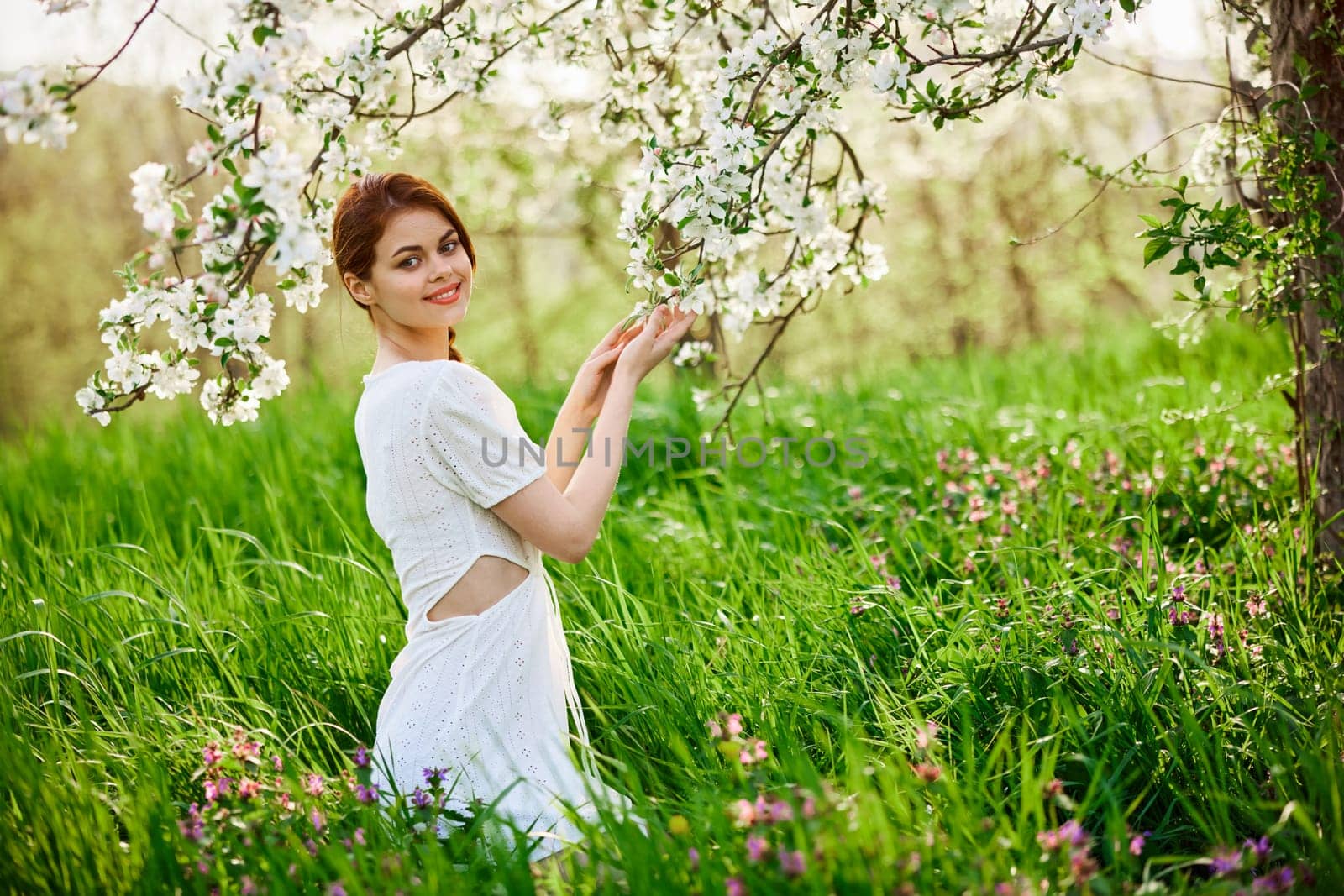 Beautiful woman in a blooming spring garden in a light dress smiling looking at the camera by Vichizh