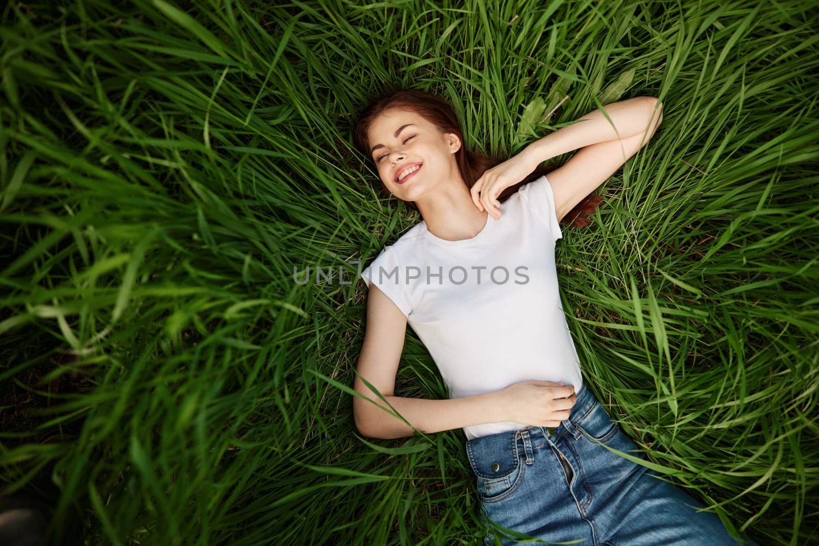 a beautiful, slender woman lies in the tall green grass in a white T-shirt. High quality photo