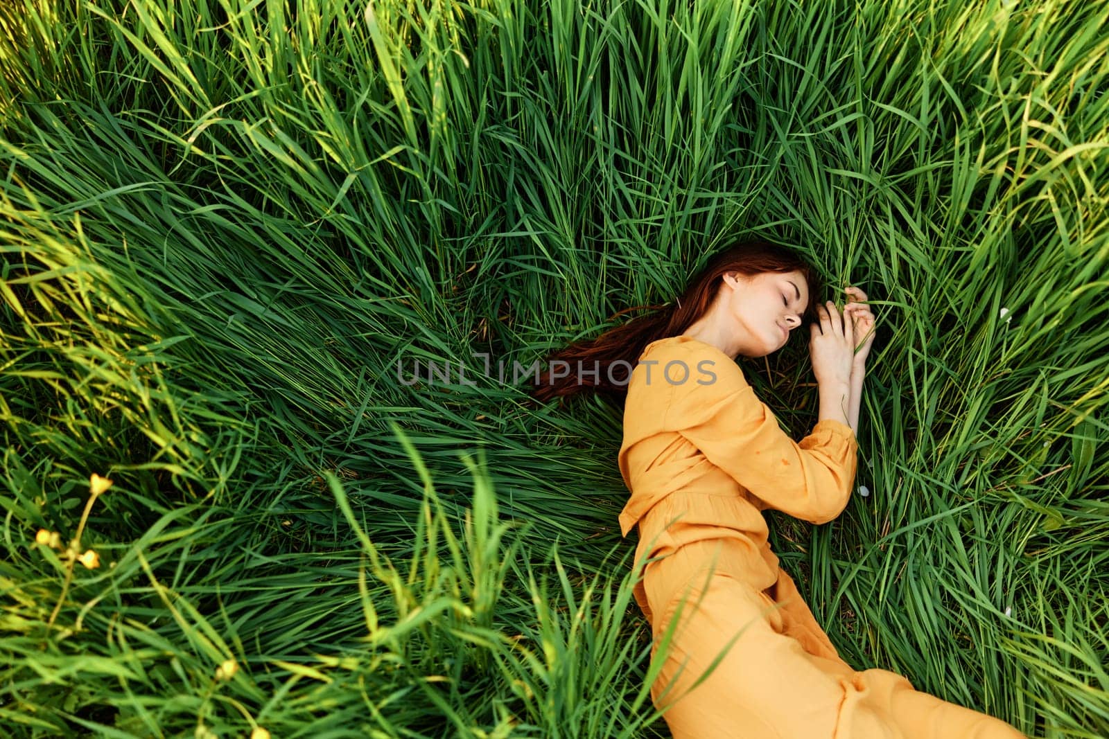 a relaxed woman enjoys summer lying in the tall green grass with her eyes closed. Photo taken from above by Vichizh
