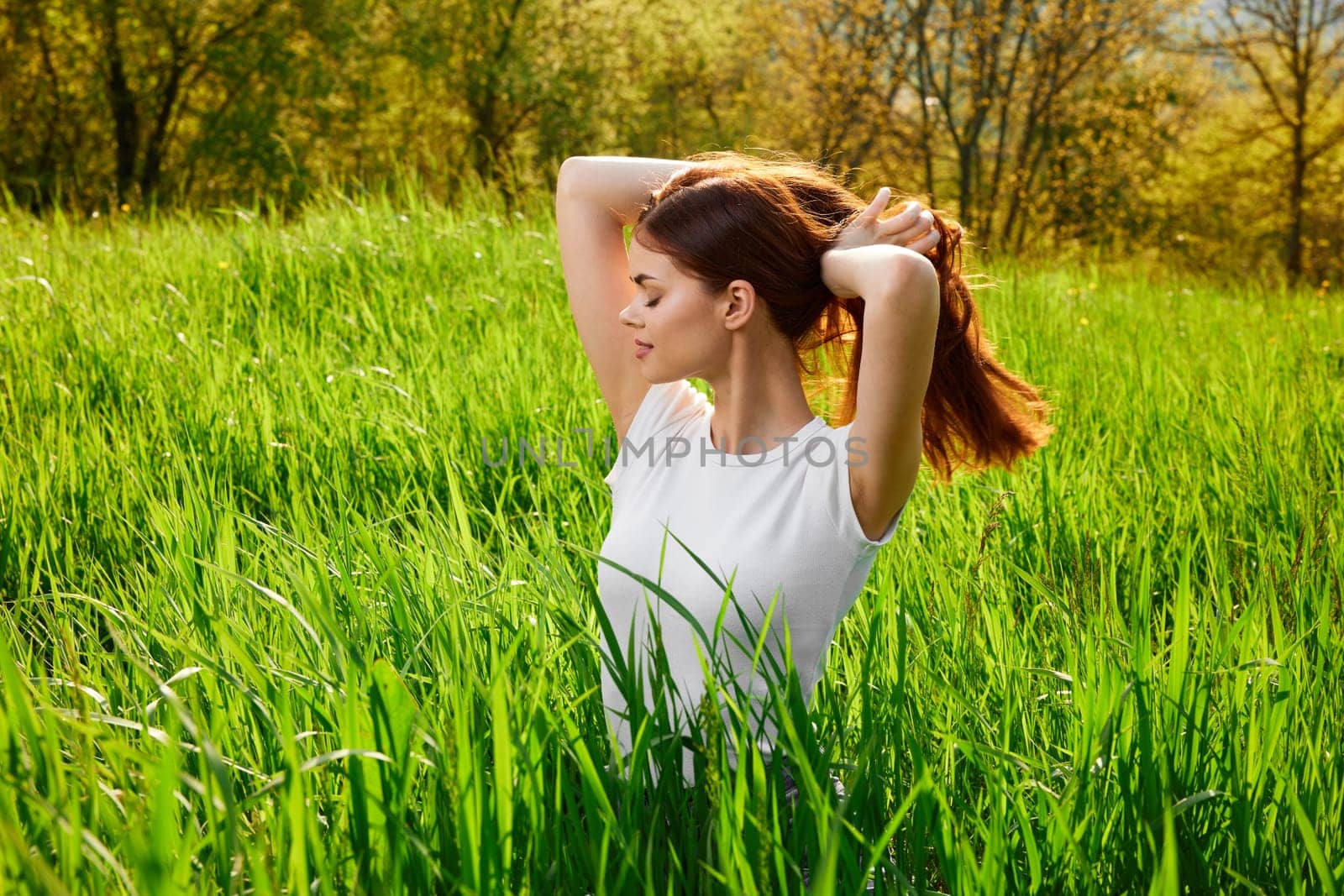 beautiful woman sitting in tall grass adjusting her hair. High quality photo