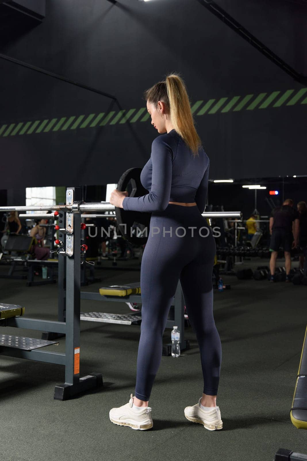 One adult caucasian woman female athlete putting weight plate on the barbel at gym. wearing blue leggins and long sleeve top