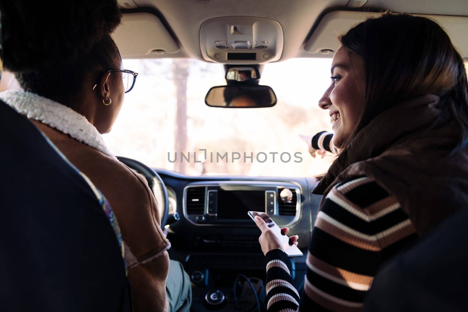 two interracial friends starting a road trip in camper van with the travel route in the phone navigation app, concept of female friendship and diversity