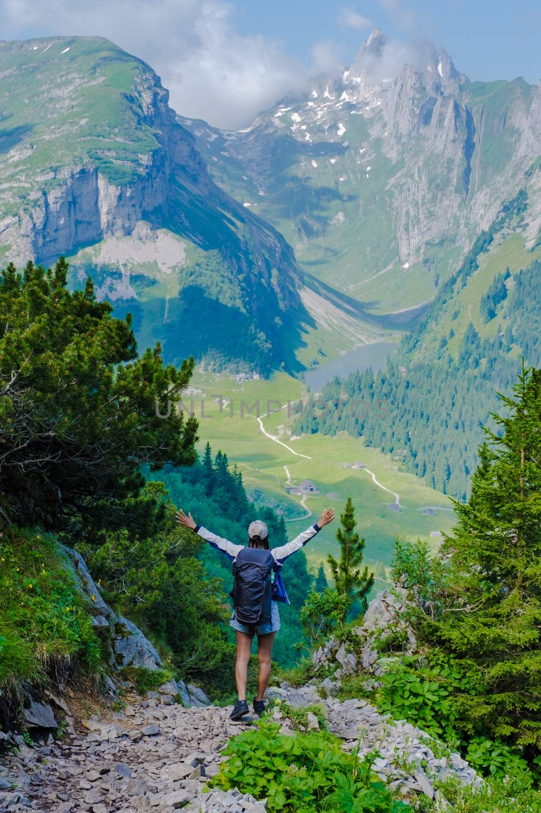 Asian women with hands up hiking in the Swiss Alps mountains during summer vacation with a backpack and hiking boots. woman walking on the Saxer Lucke path