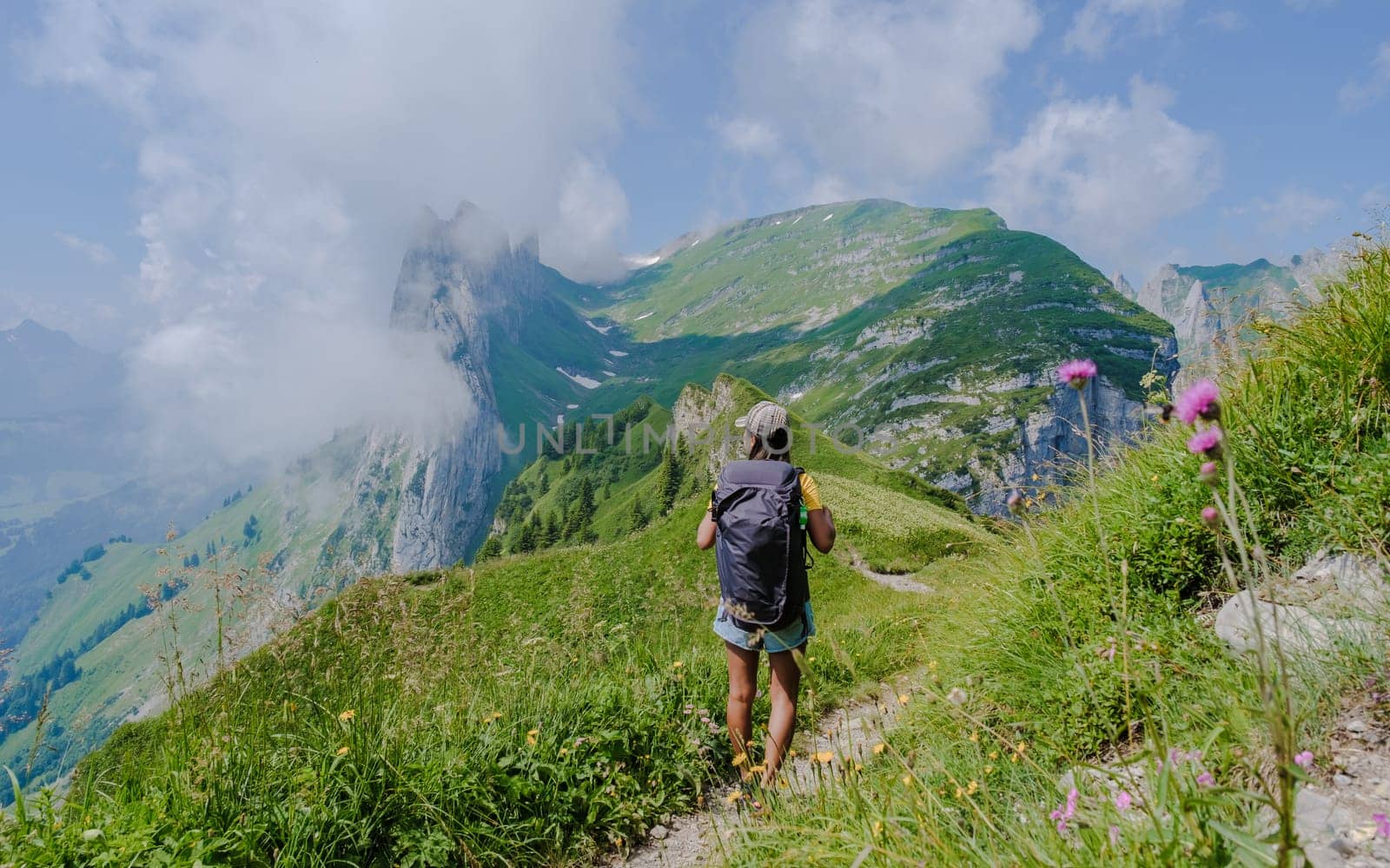 Asian women hiking in the Swiss Alps mountains at summer vacation with a backpack and hiking boots by fokkebok