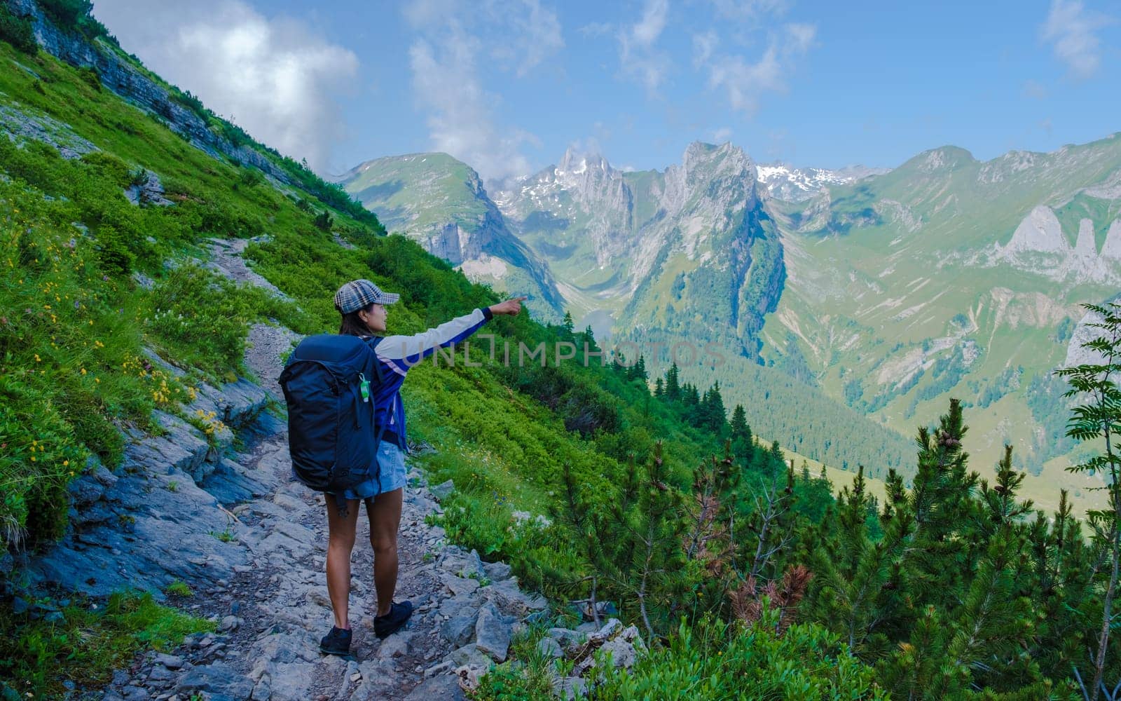 Asian women with hands up hiking in the Swiss Alps mountains during summer vacation with a backpack and hiking boots. woman walking on the Saxer Lucke path