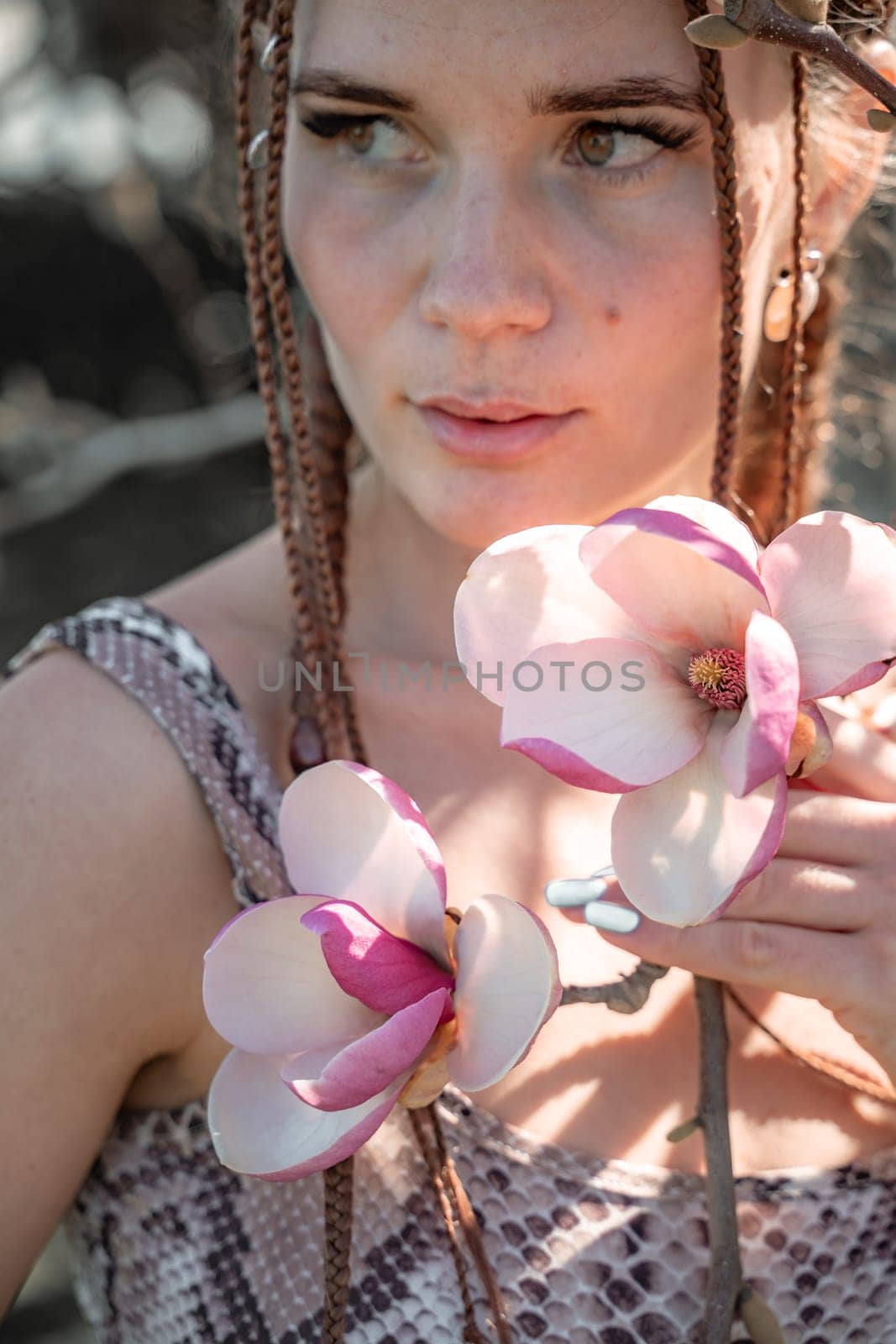 Magnolia flowers. Happy woman enjoys by blooming magnolia tree and sniffs it flowers with closed eyes in spring garden. Portrait