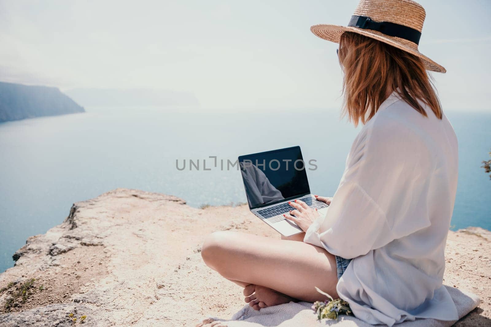 Woman sea laptop. Successful business woman working on laptop by the sea. Pretty lady typing on computer at summer day outdoors. Freelance, digital nomad, travel and holidays concept. by panophotograph