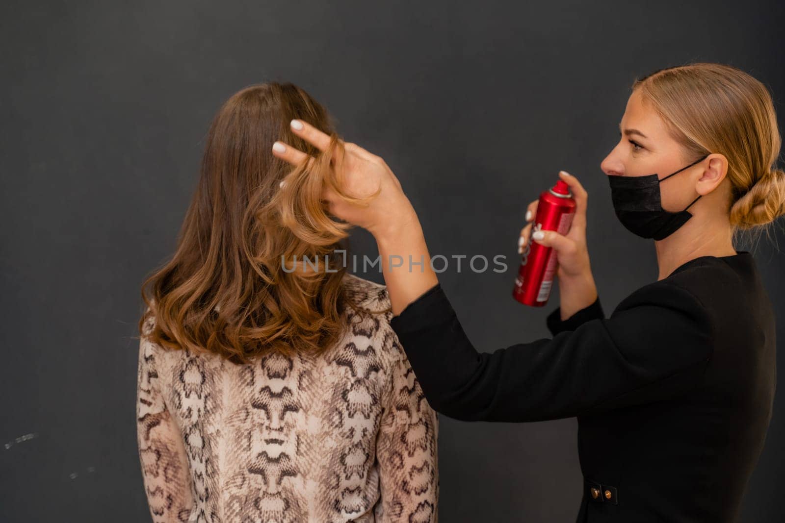 Women salon hairstyle. Hairdresser uses hairspray on client's hair in salon, Portrait of two beautiful women.