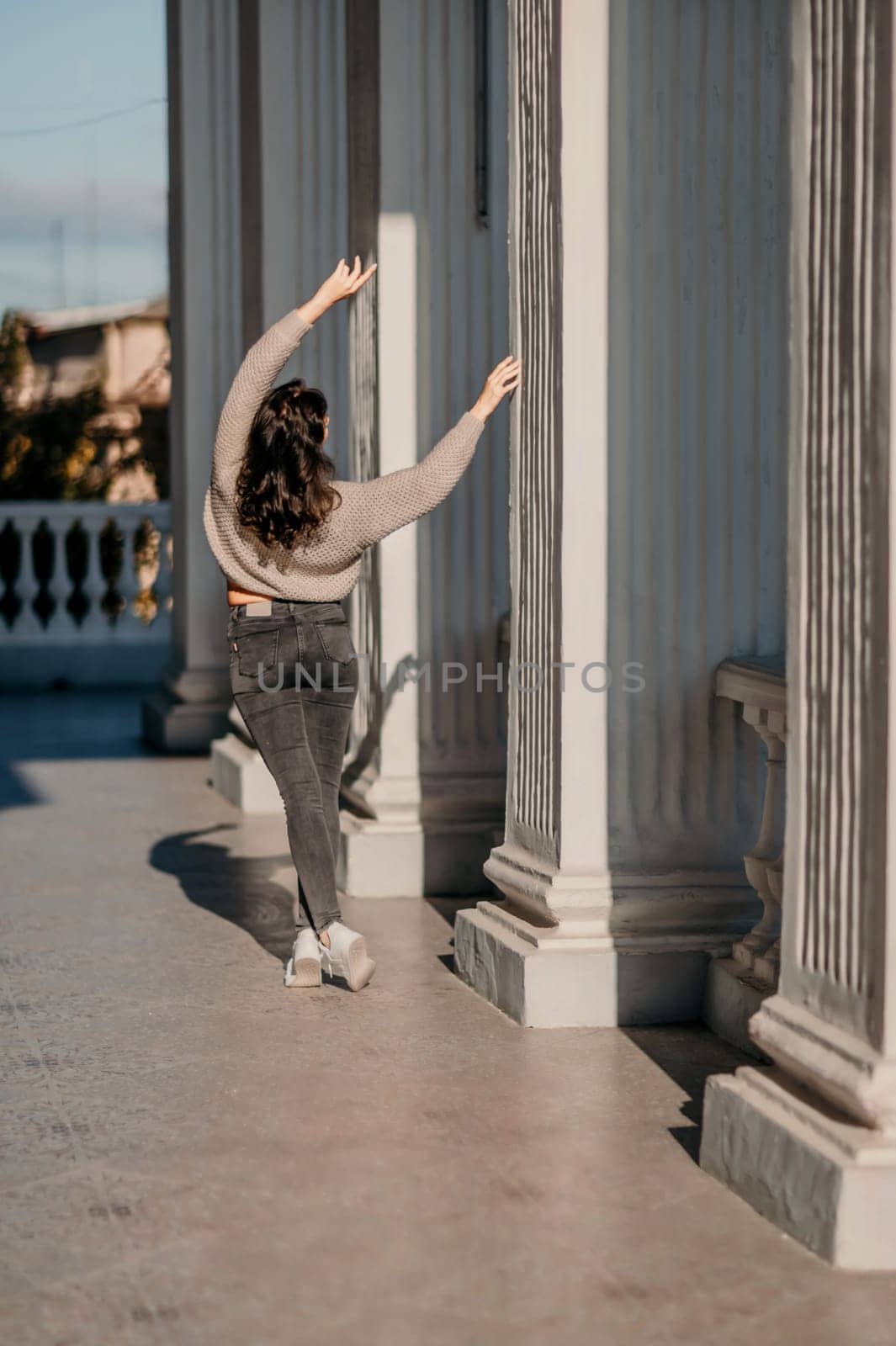 Woman building columns. An athletic woman in her 40s, dressed in a beige sweater and black jeans, poses near the pillars of a building. Walking around the city, tourism. by Matiunina