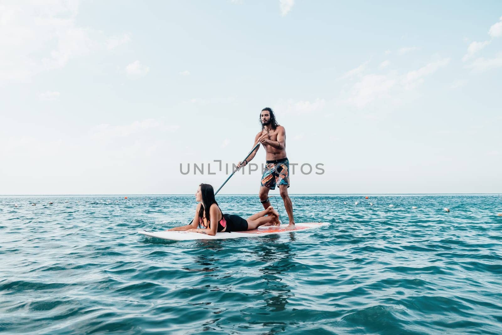 Silhouette of woman standing, surfing on SUP board, confident paddling through water surface. Idyllic sunset or sunrise. Sports active lifestyle at sea or river.