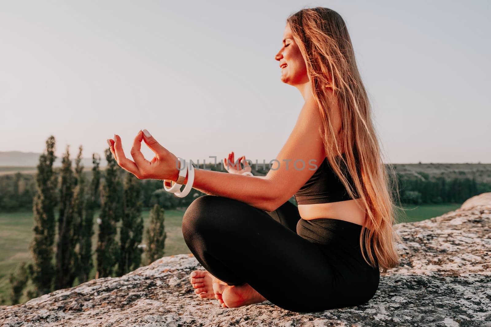 Well looking middle aged woman with long hair, fitness instructor in leggings and tops doing stretching and pilates on the rock near forest. Female fitness yoga routine concept. Healthy lifestyle.