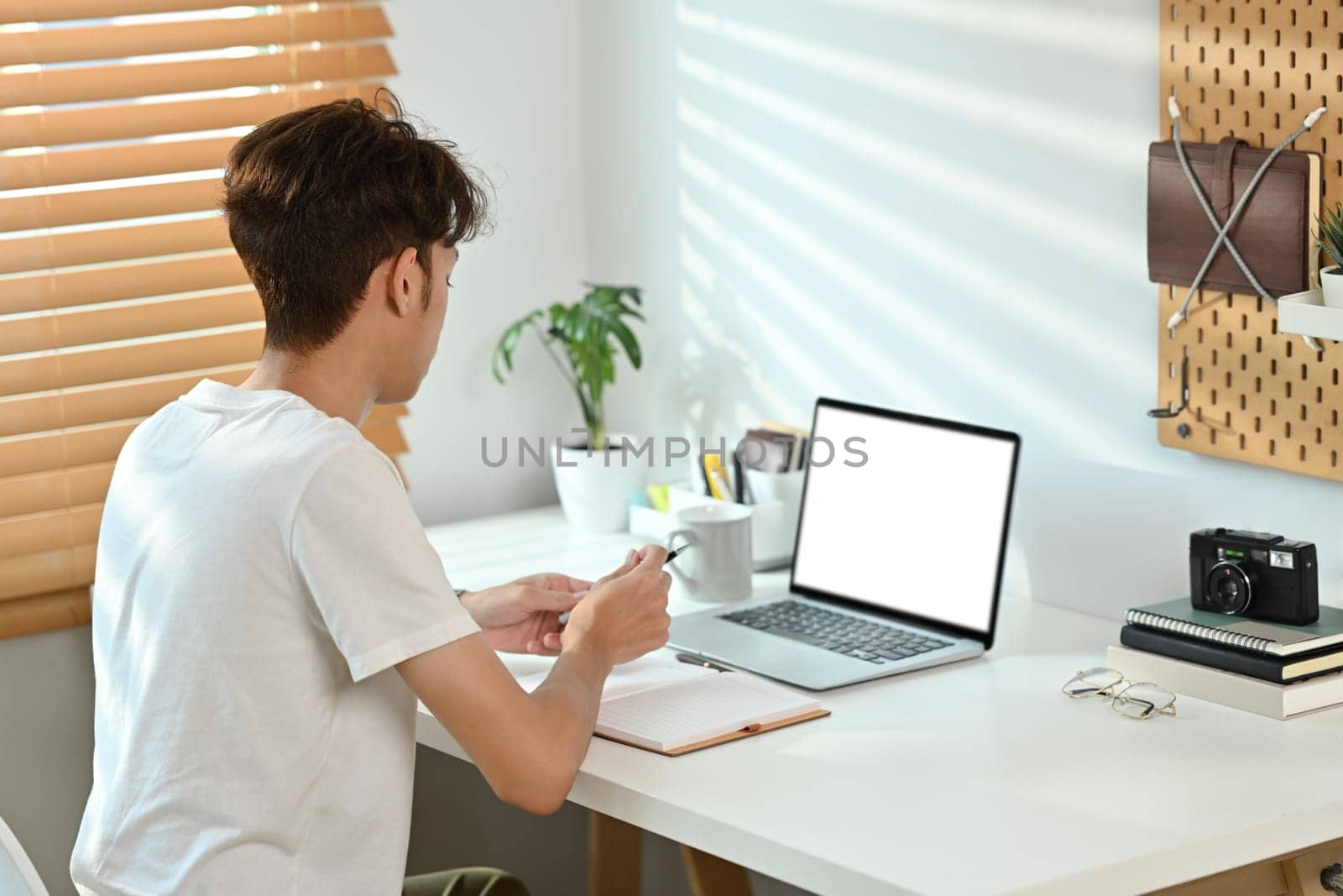 Back view of man in casual outfit using laptop computer at home. Freelance, creative occupation, e-learning concept.