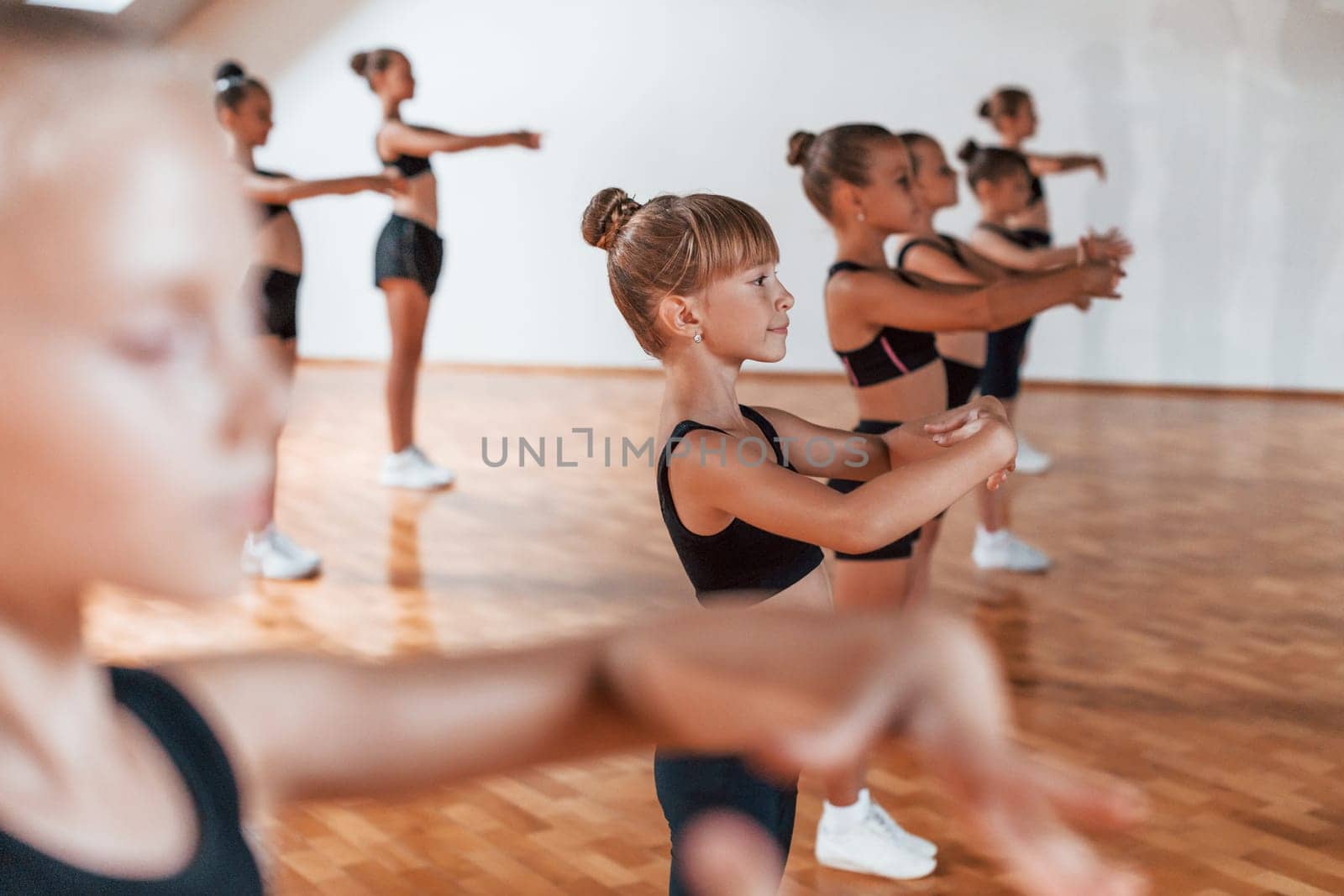 Standing in the row. Group of female kids practicing athletic exercises together indoors by Standret