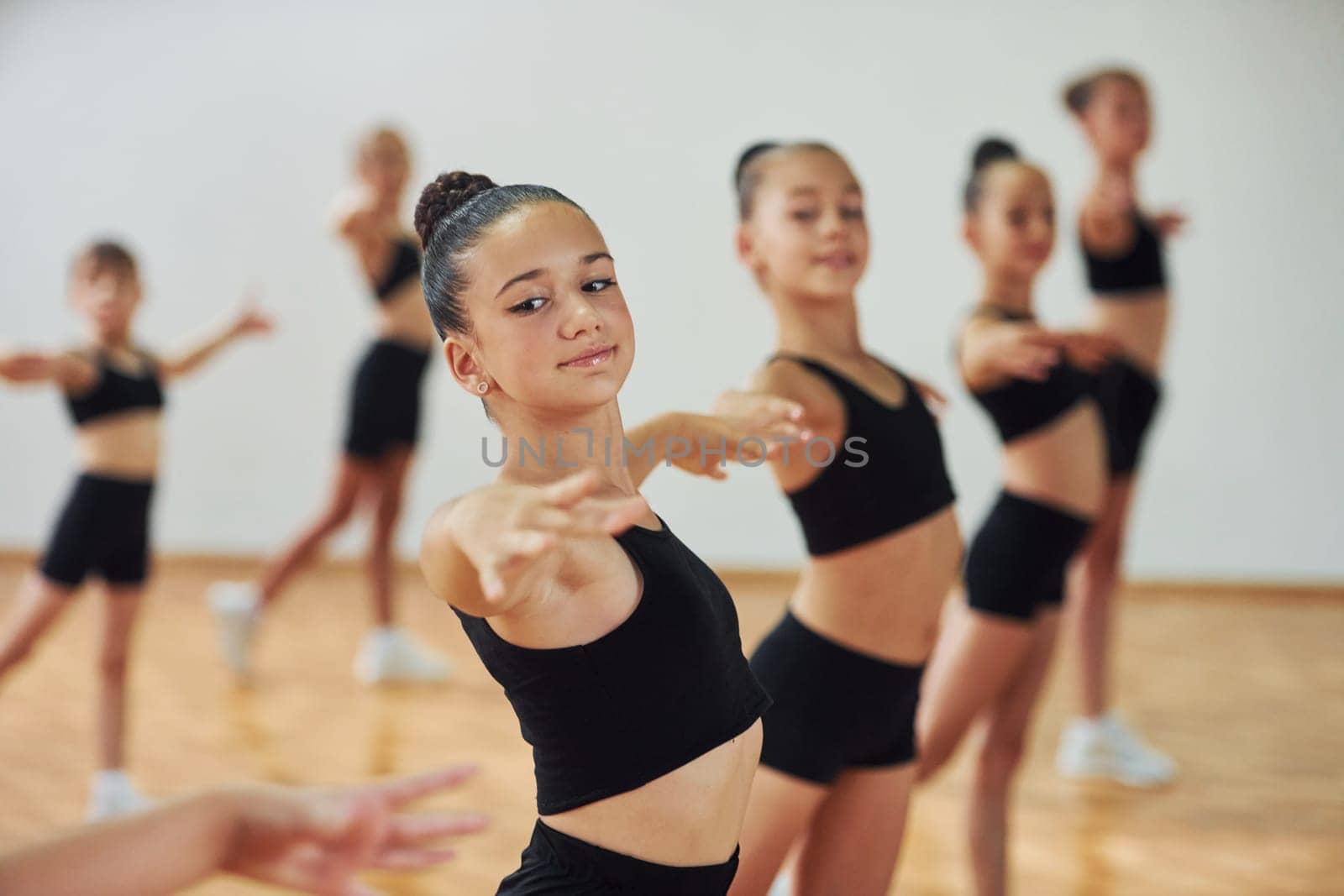 Standing and doing synchronised moves. Group of female kids practicing athletic exercises together indoors by Standret