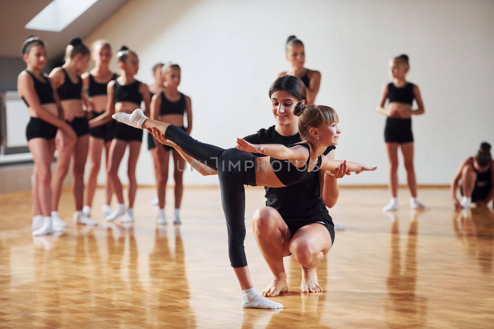 Woman teaching and helping. Group of female kids practicing athletic exercises together indoors by Standret