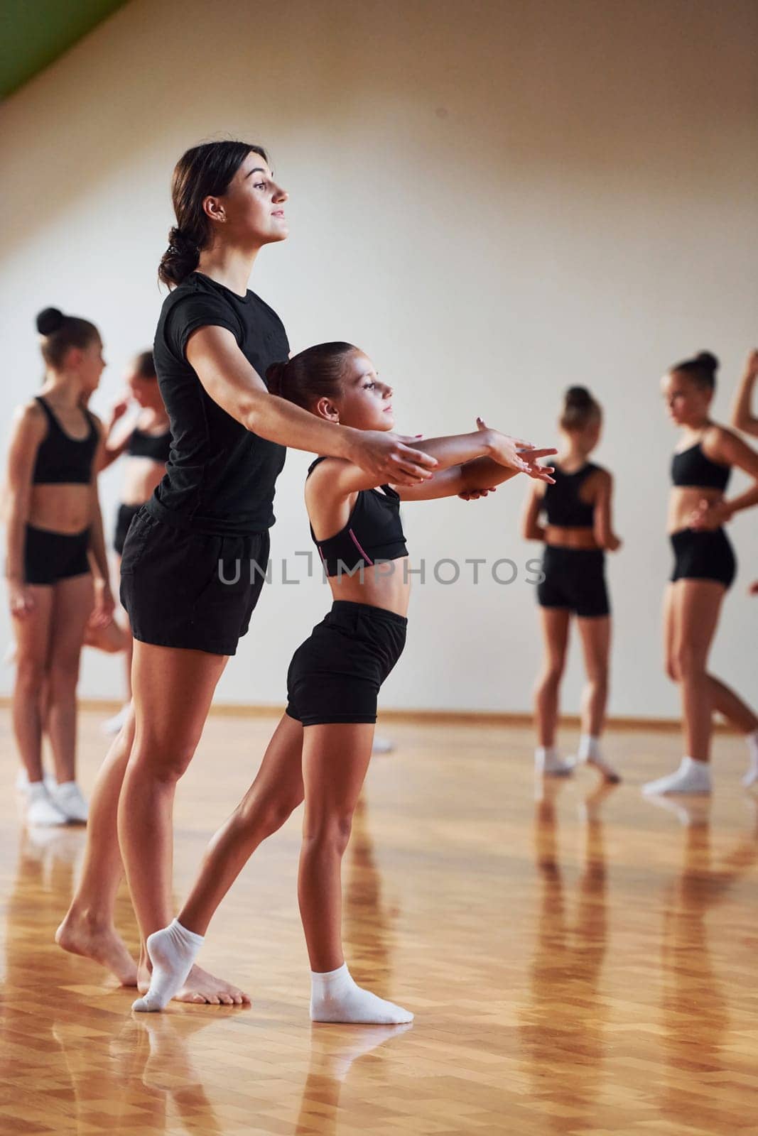 Woman teaching and helping. Group of female kids practicing athletic exercises together indoors.