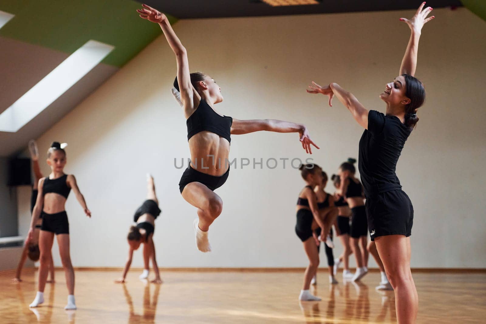 Woman teaching and helping. Group of female kids practicing athletic exercises together indoors by Standret