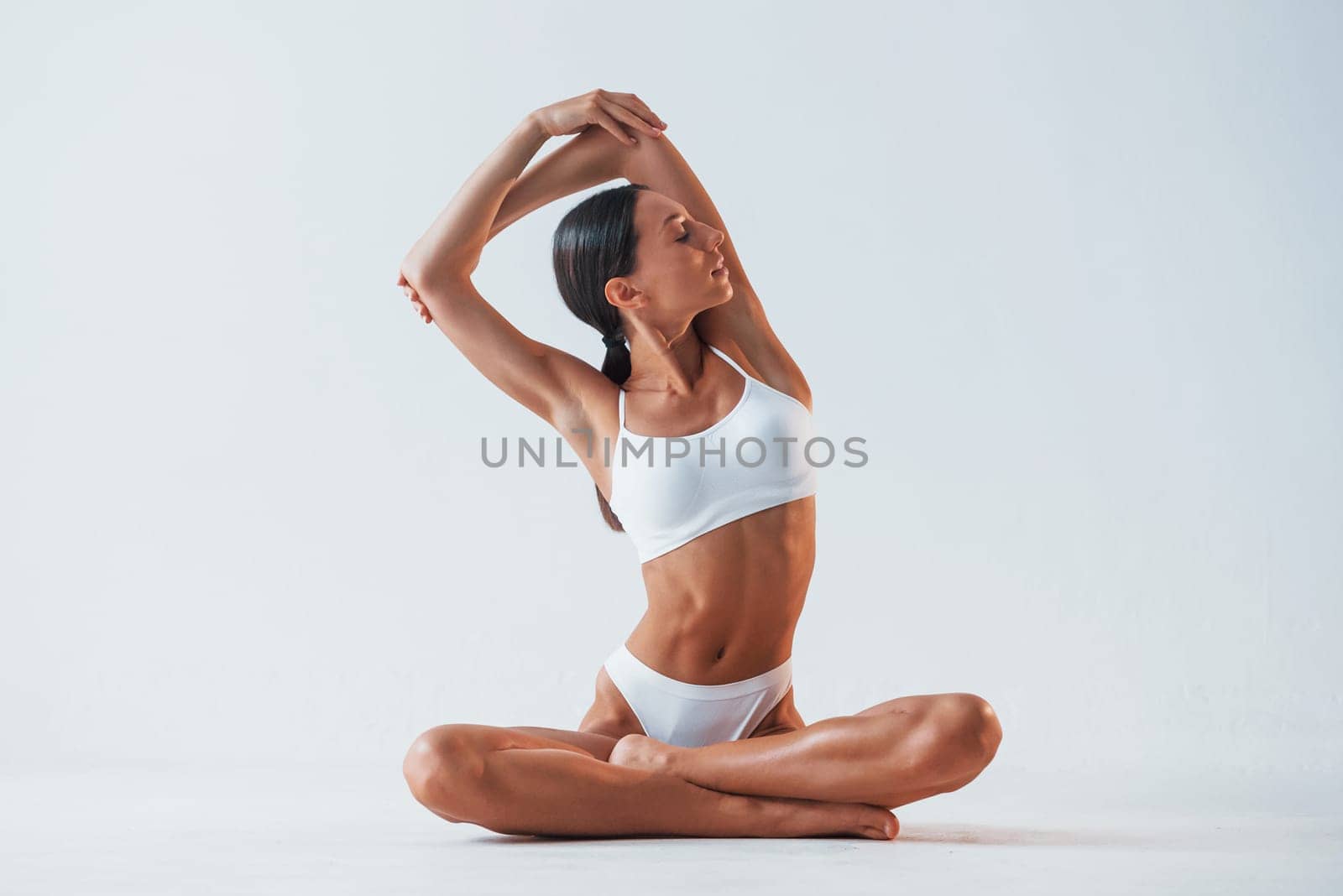 Doing exercises. Beautiful woman with slim body in underwear is in the studio.