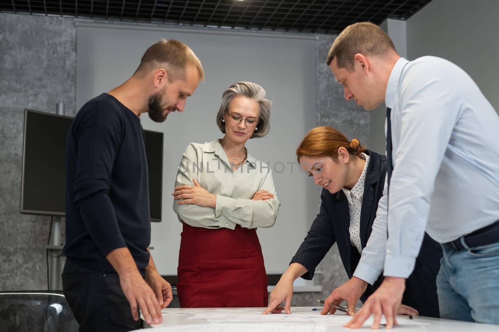 Four business people review and discuss blueprints. Designers engineers at a meeting