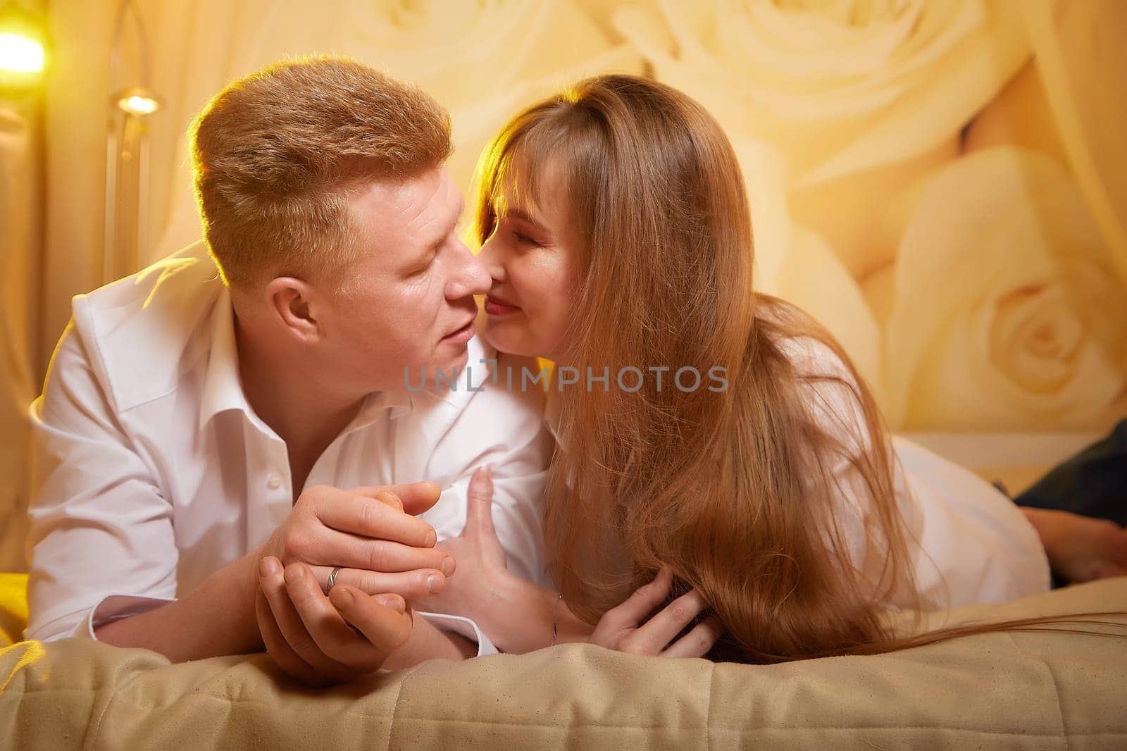 An adult couple of newlyweds in in white shirts in a hotel room after the wedding. A guy and a girl, a man and a woman in a beautiful room. The concept of love and care by keleny