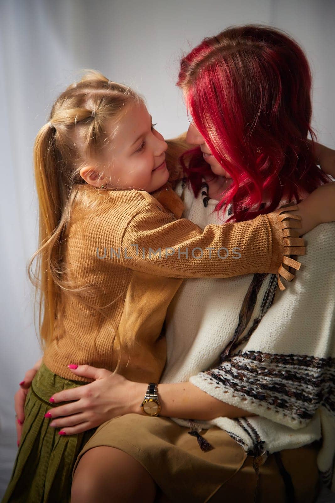 Amazing pretty mother and daughter having fun together. Red haired mom and small little blonde girl hugging and having lovely free time on white background by keleny