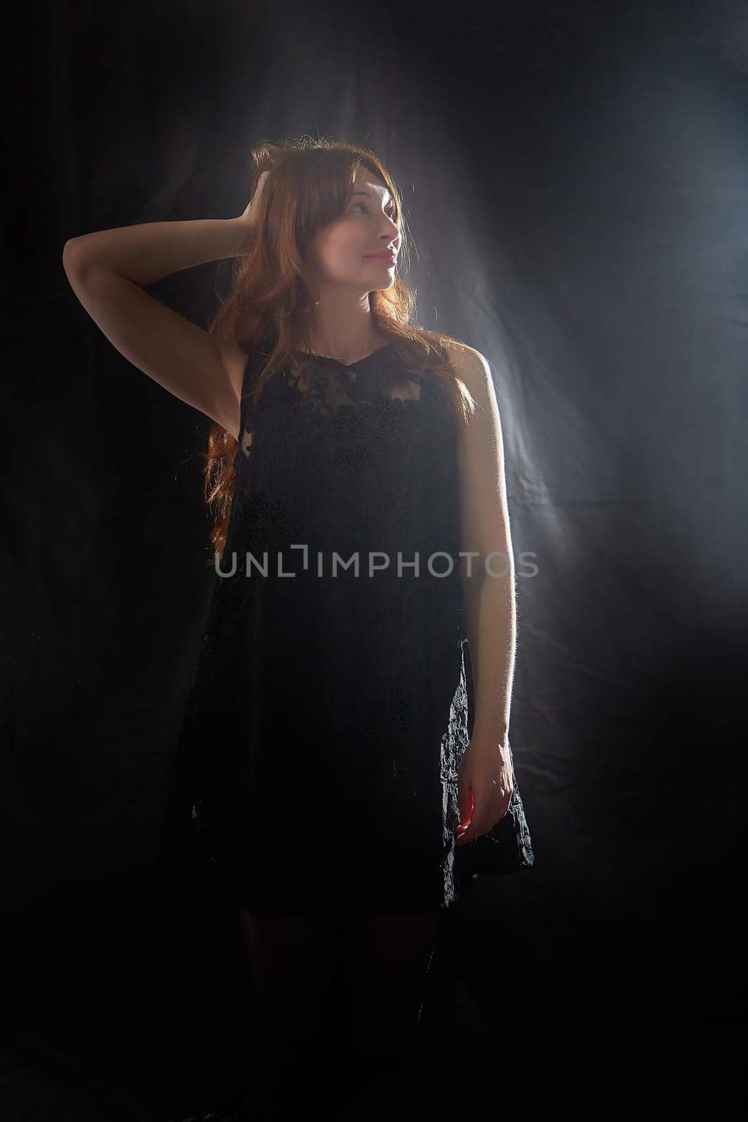 Fashion studio portrait of young beautiful female model in short black sexy dress on textile background with flash. Glamour photo of pretty girl with slim figure by keleny