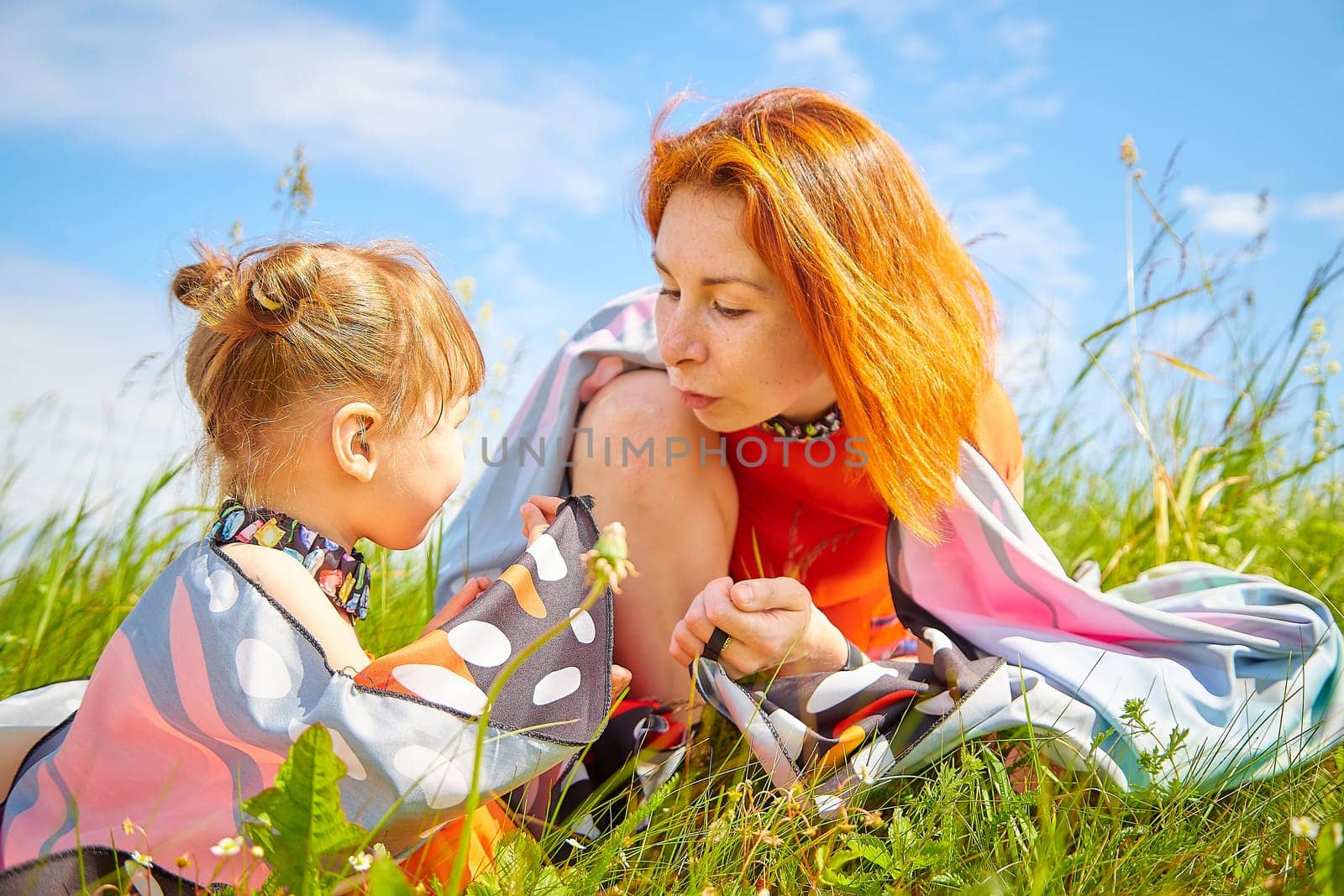 Happy female family with mother and daughter on green and yellow meadow full of grass and flower. Woman with red hair and blonde girl having fun, joy and hug in sunny summer day. Concept family love