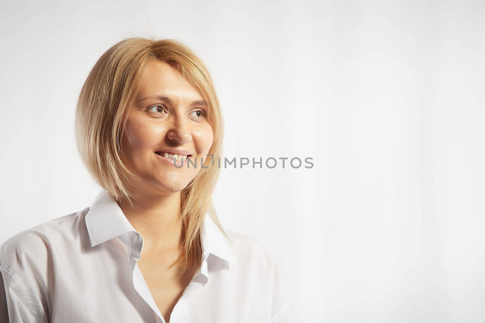 Portrait of a pretty blonde smiling woman posing on white background. Happy girl model in white shirt posing in studio. Copy space