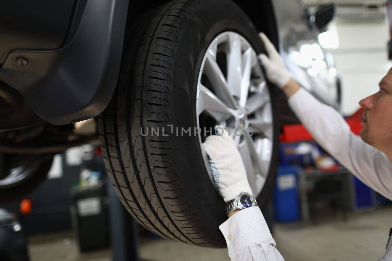 Auto mechanic in car repair shop inspects the wheels and suspension of car on lift by kuprevich