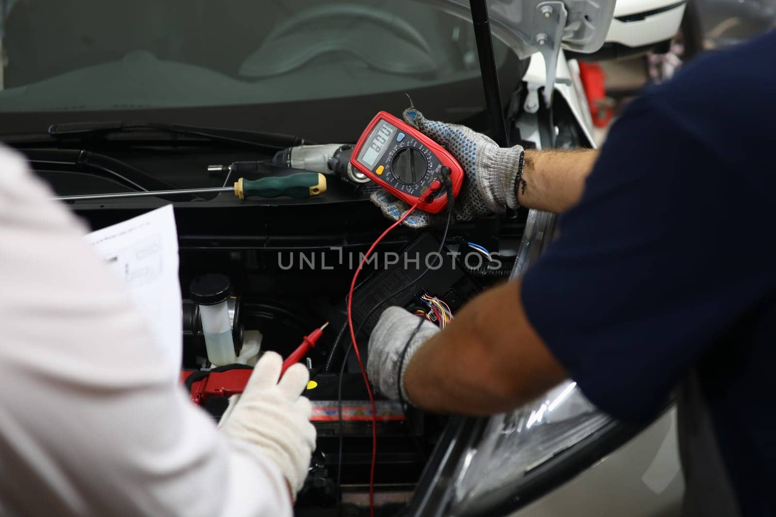 Car repairman checking and testing car battery with digital electronic tester. Car electrical analyzer in car repair shop