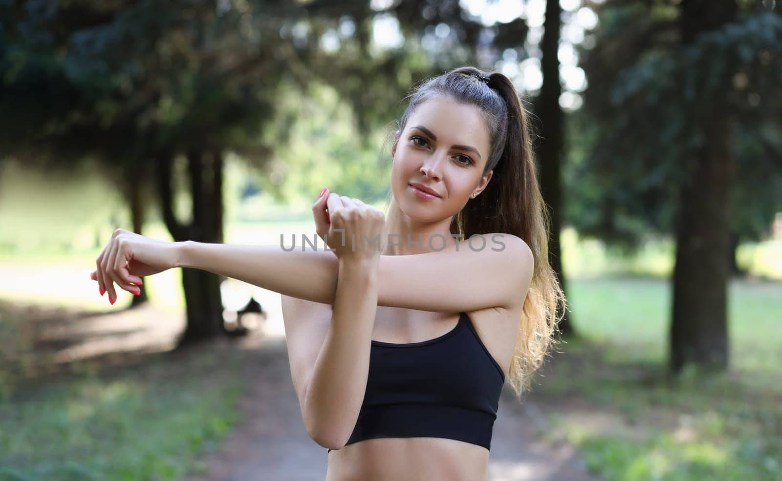 Portrait of beautiful sports woman stretches arms in park by kuprevich