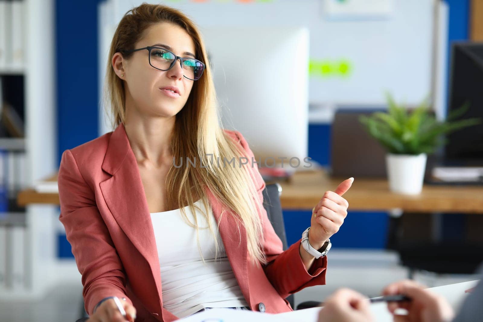 Stylish businesswoman in glasses talking to colleague at workplace by kuprevich