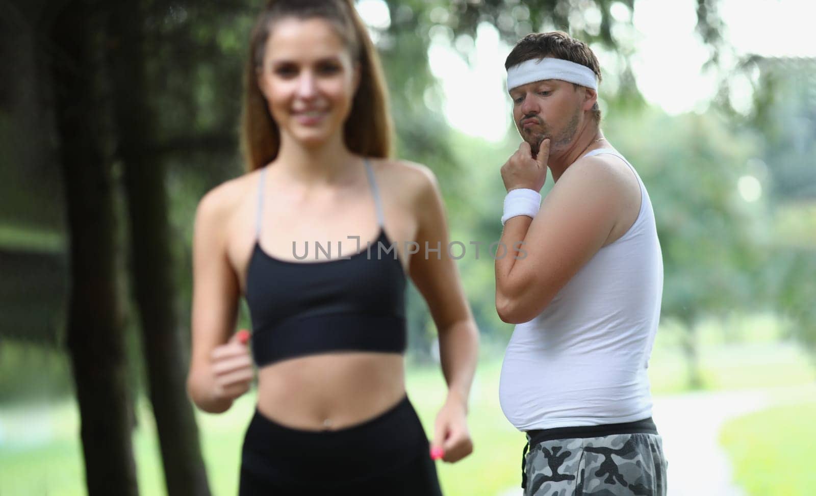 Man emotionally looks at beautiful athletic girl in park. Man jealous of woman athletic body in park