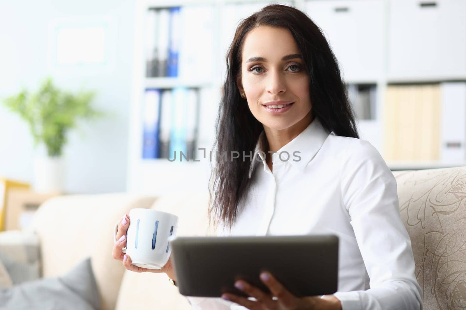 Portrait of a beautiful woman with tablet and cup on sofa. Applications for business and planning the working day
