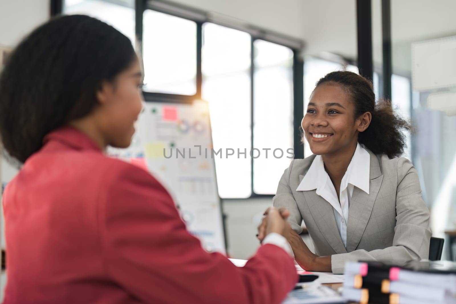 Positive businesswomen shaking hands in meeting room.