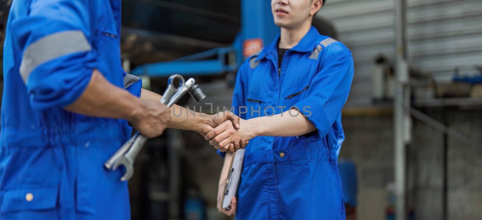 Two car mechanic team shaking hand at automobile service center. Repair service concept. Car repair and maintenance. Car mechanic working at automotive team service center by wichayada