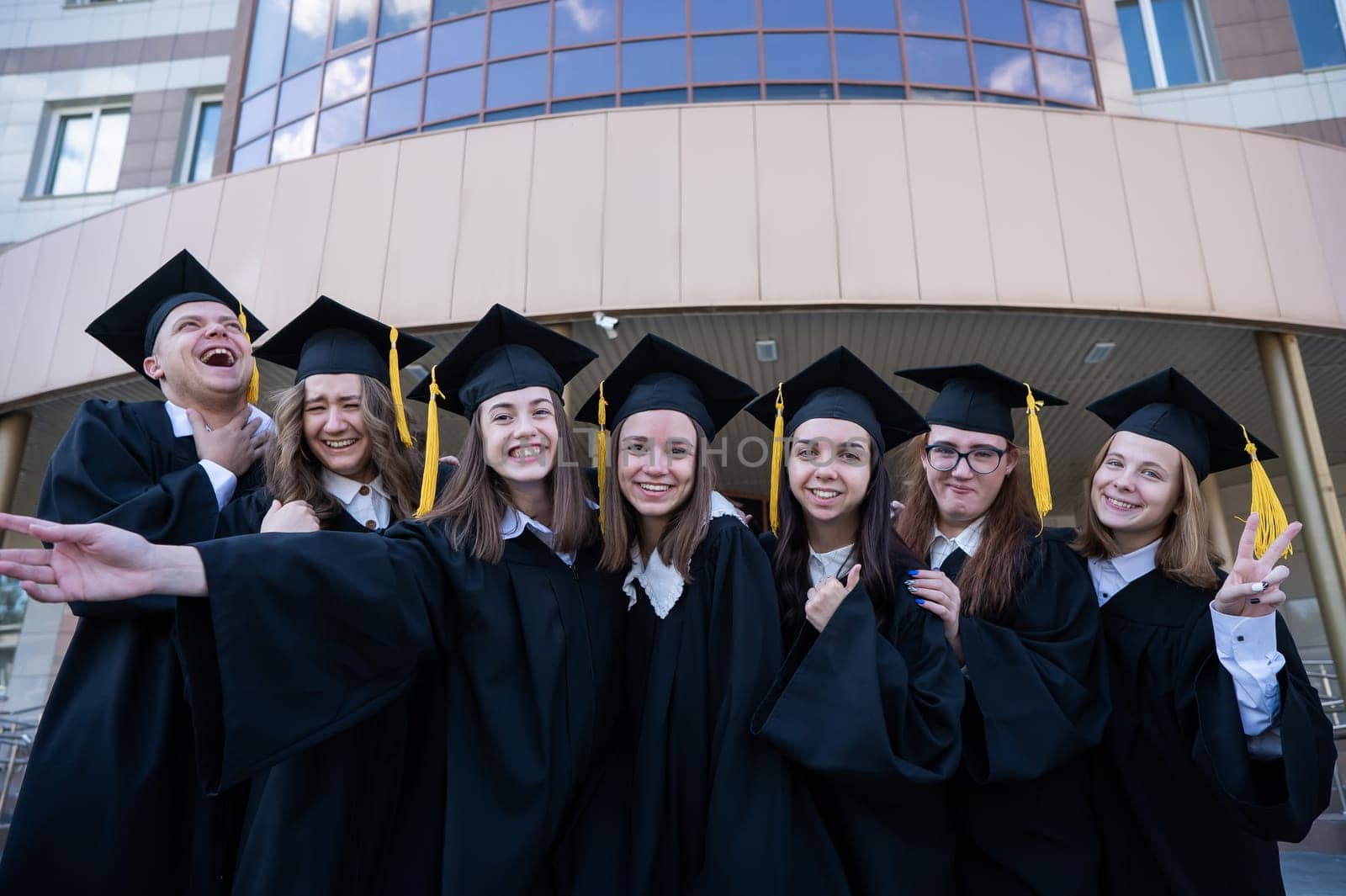 Happy students in graduate gown stand in a row against the backdrop of the university. by mrwed54