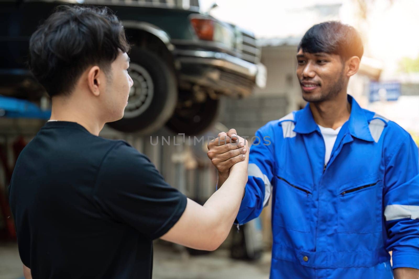 Two car mechanic team shaking hand at automobile service center. Repair service concept. Car repair and maintenance. Car mechanic working at automotive team service center by wichayada