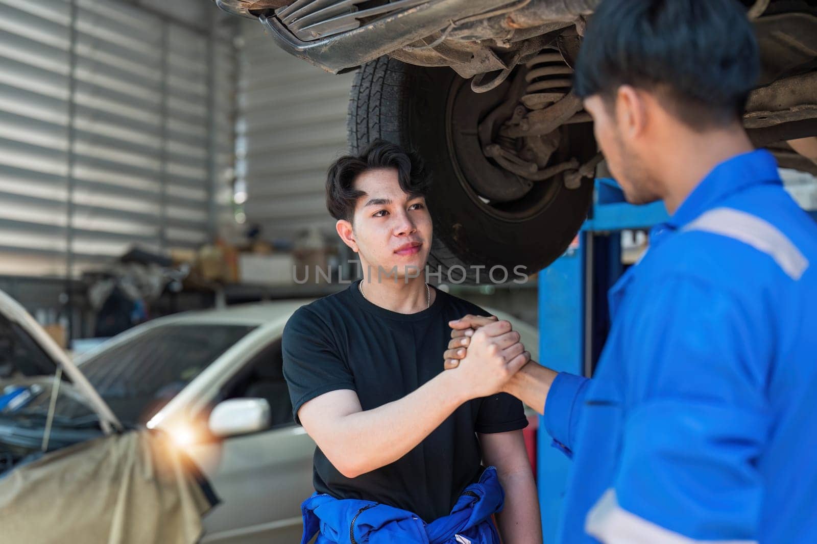 Two car mechanic team shaking hand at automobile service center. Repair service concept. Car repair and maintenance. Car mechanic working at automotive team service center by wichayada