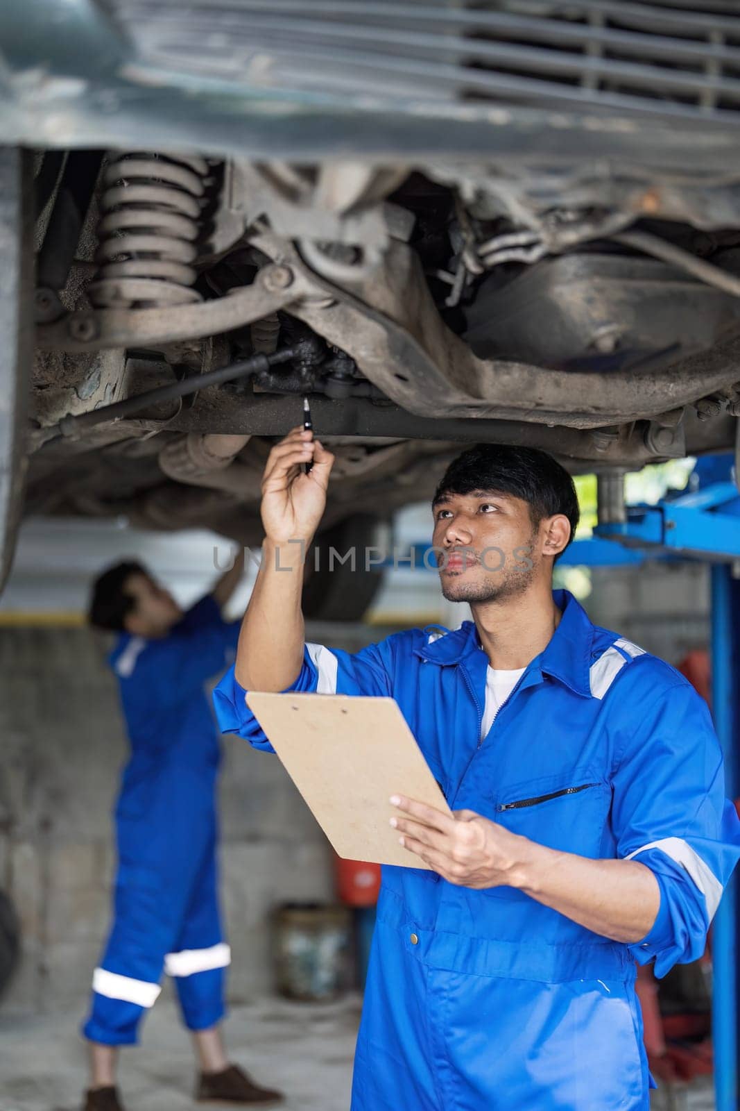 Portrait Shot of a Handsome Mechanic Working on a Vehicle in a Car Service. Professional Repairman is use a Ratchet Underneath the Car. Modern Clean Workshop. by wichayada