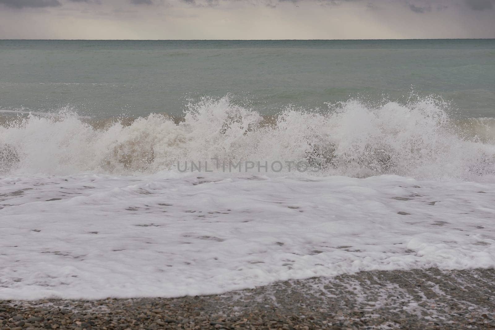 Waves breaking on the shore on small pebble beach. Storm clouds sky, turquoise water, waves,