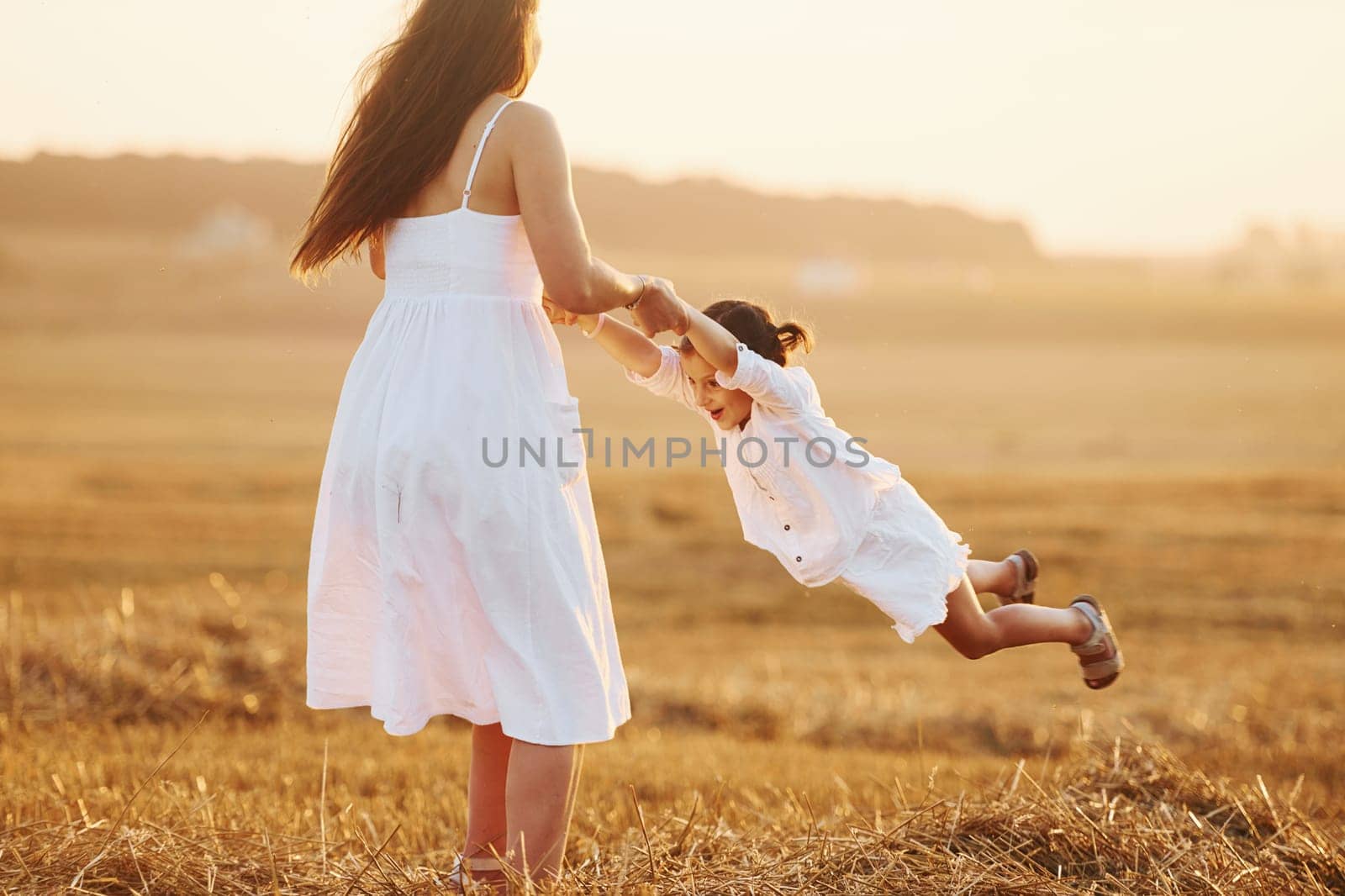 Positive little girl with her mother have weekend outdoors on the summer field together.