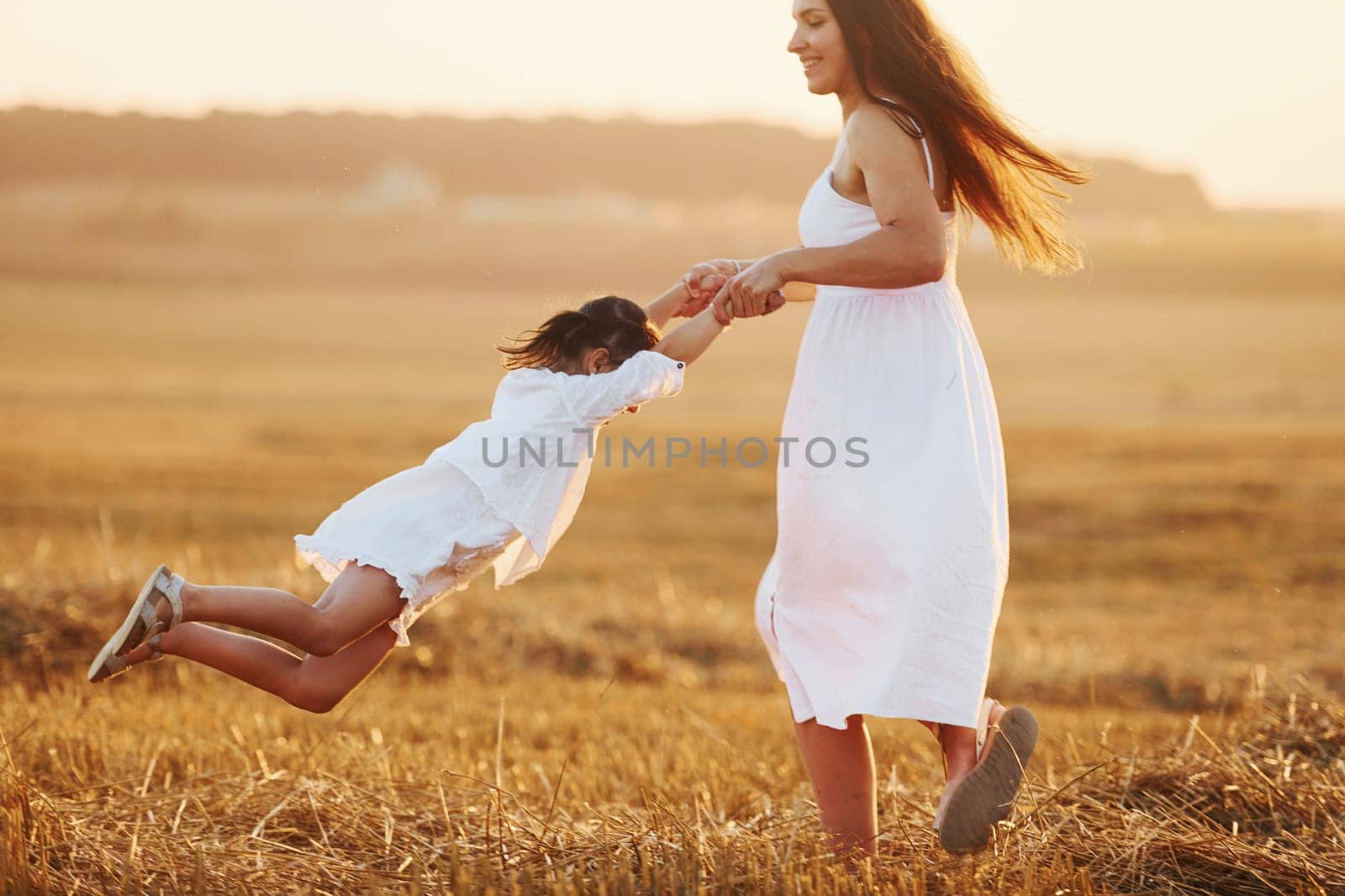 Positive little girl with her mother have weekend outdoors on the summer field together.