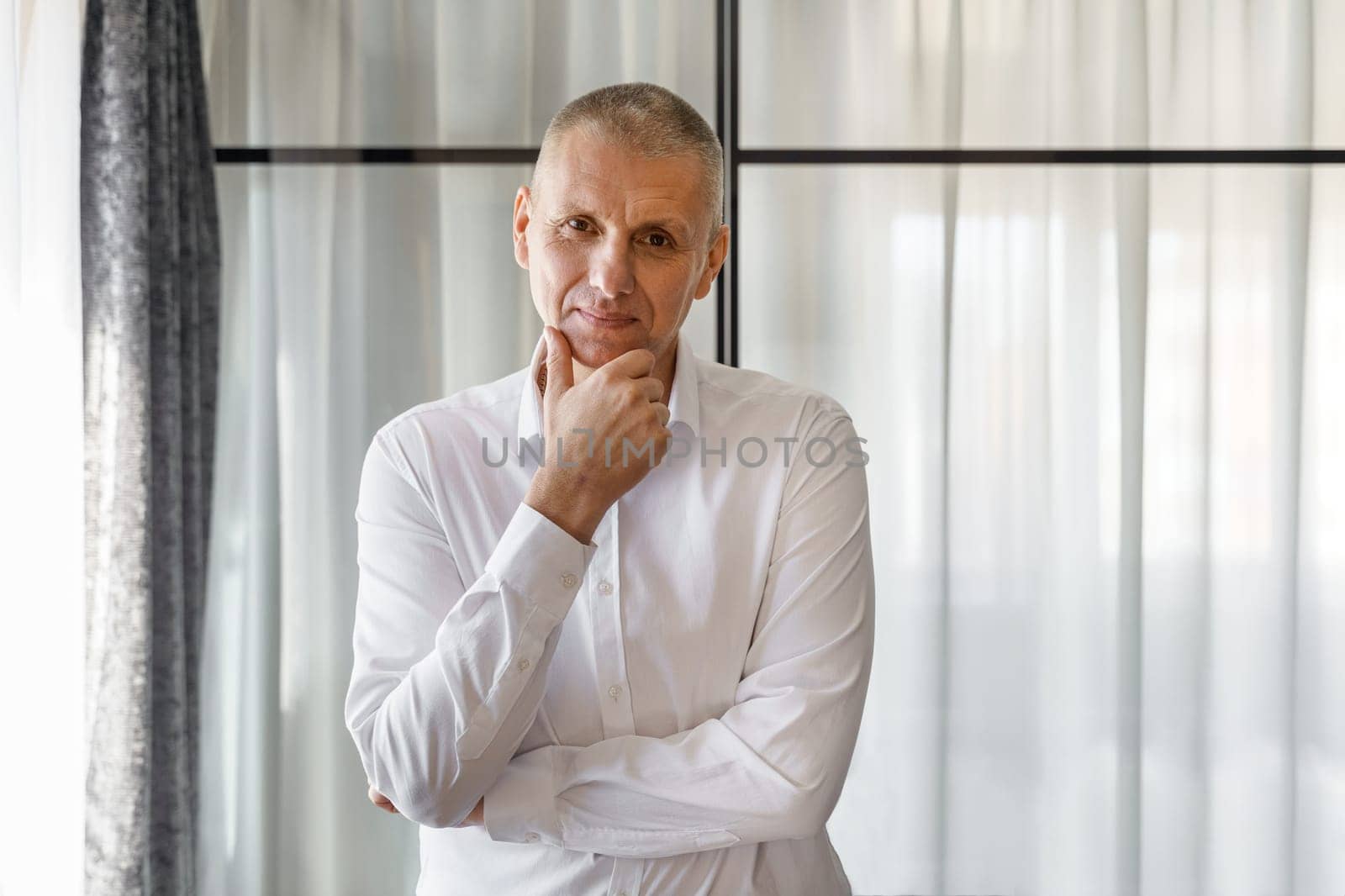 Portrait of a smiling businessman in a white shirt who is posing holding his hand to his face.