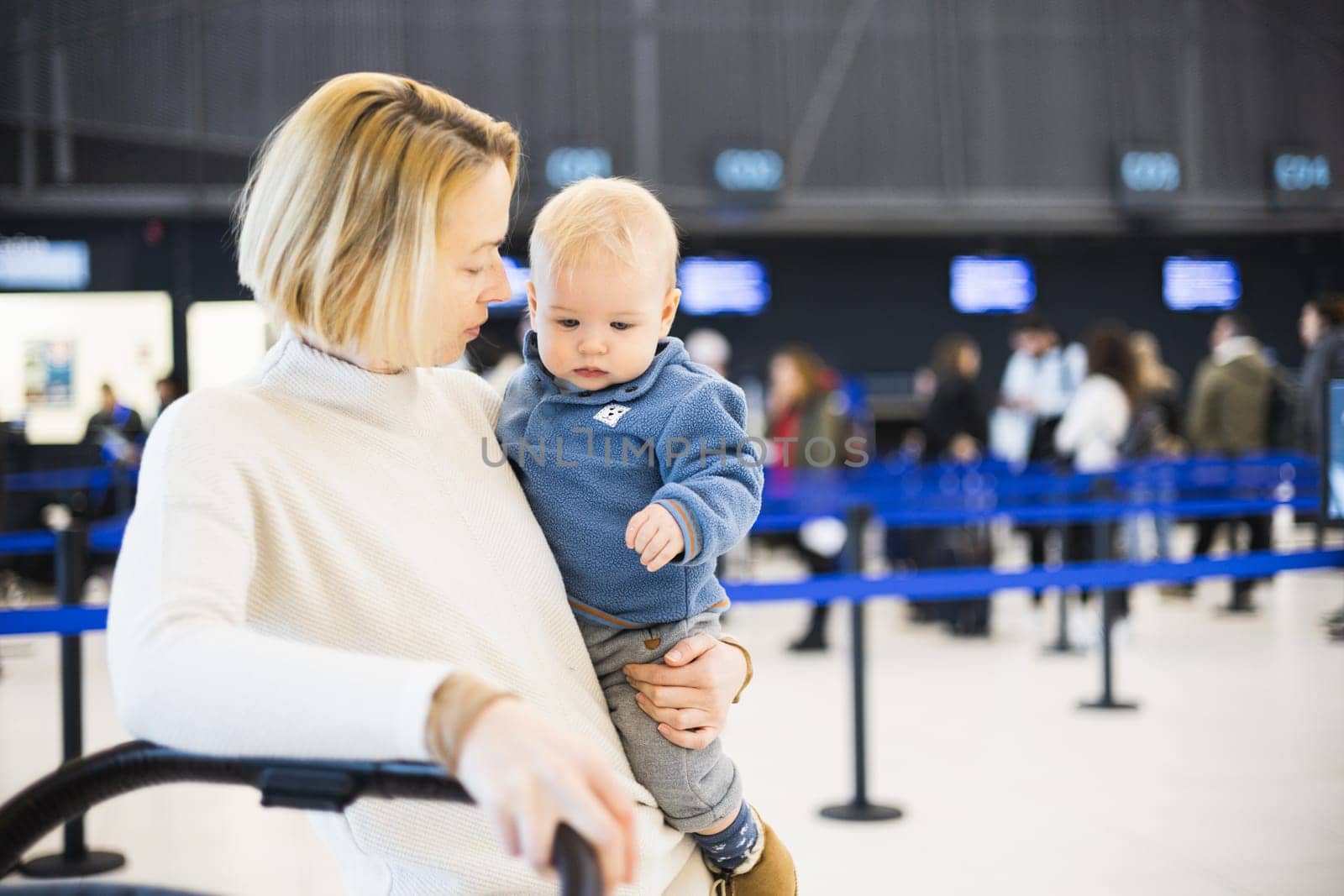 Motherat travelling with his infant baby boy child, walking, pushing baby stroller and luggage cart at airport terminal station. Travel with child concept. by kasto