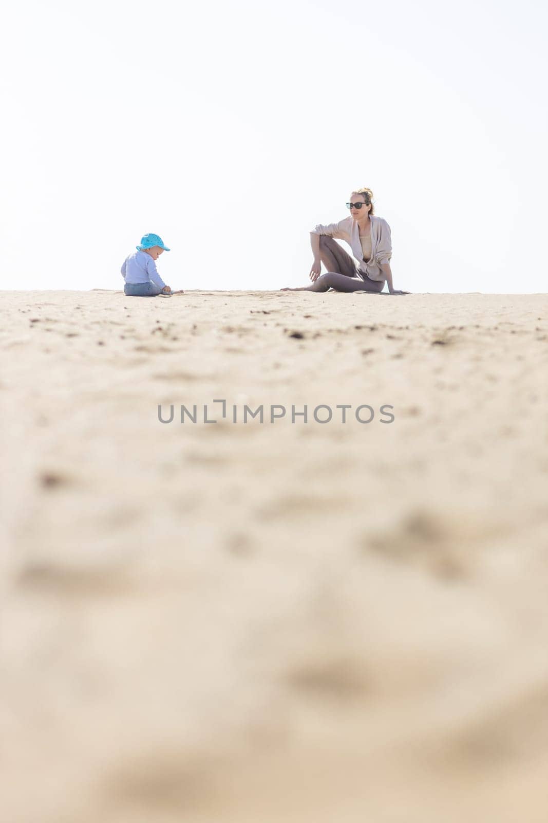 Mother playing his infant baby boy son on sandy beach enjoying summer vacationson on Lanzarote island, Spain. Family travel and vacations concept. Copy space.
